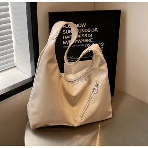 Close-up of cream textured leather tote bag showing slanted zipper and metal ring detail