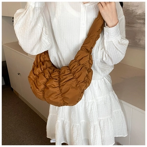 Detailansicht der karamellbraunen Cloud-Tasche mit Falten an Model in weißem Kleid