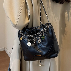 Sac seau matelassé noir avec chaîne dorée et breloques cœur porté sur un manteau beige