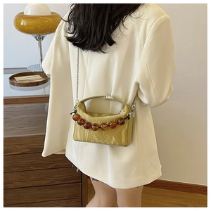 Detail van gele geplooide crossbodytas met amberkleurige kralen en kettingriem
