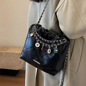 Sac seau noir matelassé avec pendentifs cœur et bandoulière chaîne sur un trench