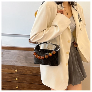 Detail van een zwarte geplooide crossbodytas met grote amberkleurige kralen en ketting