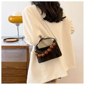 Detail van een zwarte geplooide crossbodytas met barnsteen kraalhandvat en zilveren ketting