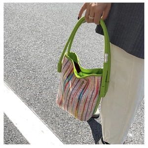 Detail of colorful striped woven bucket bag with vibrant green leather handles