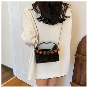 Detail van zwarte geplooide crossbodytas met amberkleurige kralen op een ivoren blazer