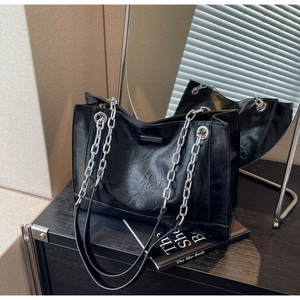 Detailansicht der schwarzen Lackledertasche mit silberner Kette und Logo-Plakette aus Metall