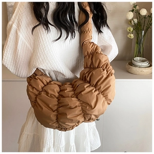 Makro-Detail der braunen Croissant-Tasche mit Faltenstruktur auf weißem Kleid