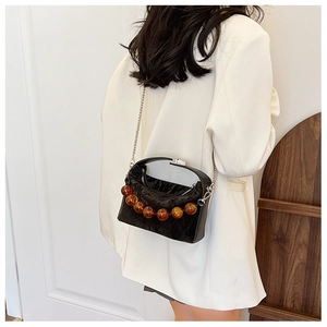 Detail van een zwarte geplooide crossbodytas met amberkleurige kralen op een witte blazer