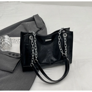 Detail der schwarzen Plissee-Tote-Bag mit Silberkette auf grauem Blazer-Hintergrund
