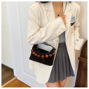 Detail van zwarte geplooide crossbodytas met amberkleurige kralen en zilveren ketting