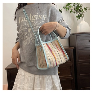 Detalle del bolso tipo cubo con rayas tejidas de colores y correas ajustables en azul claro