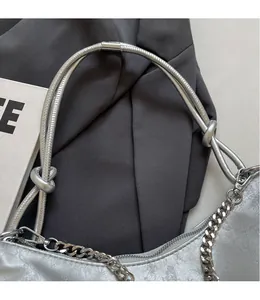 Detail of silver metallic underarm bag showing knotted strap and chunky chain hardware