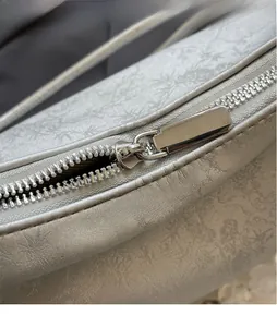 Close-up of a silver metal zipper on a gray jacquard fabric shoulder bag with silk texture