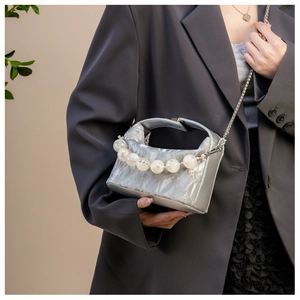 Detail van de zilveren geplooide handtas met kralenhandvat en fijne zilveren ketting