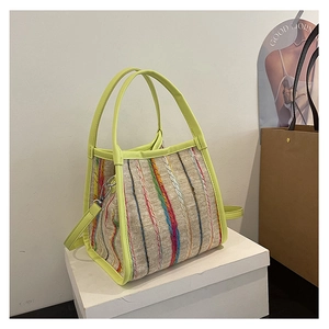 Detalle del bolso tote tejido a rayas de colores con asas de piel sintética verde neón y metal
