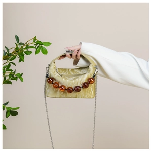 Detail van kaki crossbodytas met geplooide textuur en decoratie van amberkleurige kralen