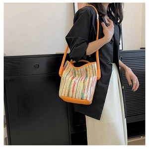 Detail of colorful striped bucket bag with orange leather handles on a female model
