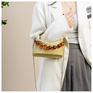 Detail van lichtgele crossbody tas met amberkleurige kralen handvat en zilveren ketting