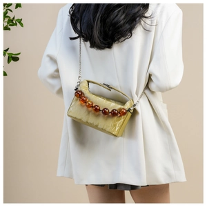 Detail van de mosterdgele geplooide crossbodytas met barnsteen kralen en metalen ketting