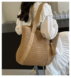 Detail of hand-woven straw tote bag with shoulder straps and decorative fringe tassel