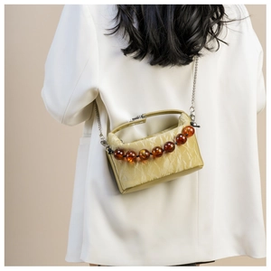 Detail van avocado groene geplooide leren tas met amberkleurige kralen en zilveren ketting