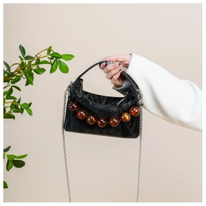 Detail van zwarte geplooide fluwelen handtas met amberkleurige kralenketting en riem