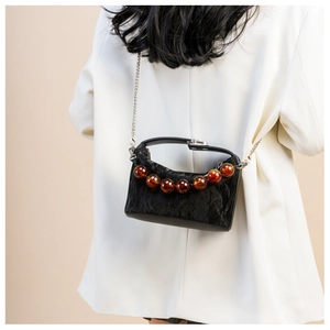 Detail van een zwarte geplooide crossbodytas met amberkleurige kralen op wit blazer model