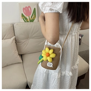 Close-up of a woven straw bucket bag featuring a bright yellow 3D flower and rope strap