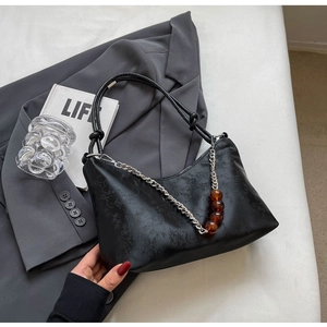 Detail of matte black shoulder bag featuring bamboo pattern and amber bead chain