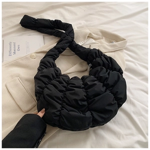 Detail der schwarzen gerafften Croissant-Tasche aus gepolstertem Nylon auf hellem Mantel