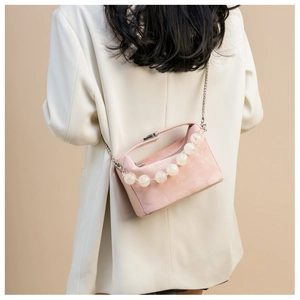 Detail van roze suède crossbodytas met grote kralen en een zilverkleurige kettingriem