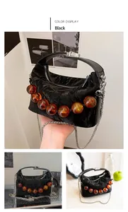 Detail van zwarte geplooide crossbodytas met amberkleurige kralen en zilveren ketting