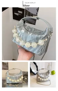 Detail van zilveren metallic geplooide handtas met grote parelketting en metalen band