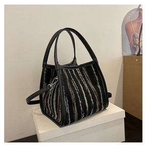 Detalle de la textura tejida a rayas y el asa de cuero negro en el bolso de mano