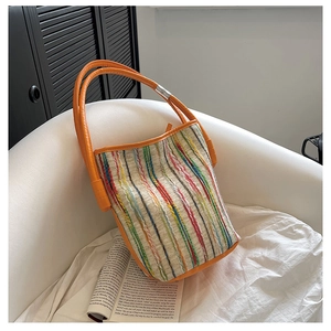 Détail d'un sac cabas tissé à rayures colorées avec des anses en cuir orange sur un fauteuil