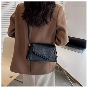 Detail of a black faux crocodile crossbody bag with V-shaped flap on a modern brown blazer
