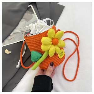 Detail of a bright orange straw bucket bag with a large yellow flower and drawstring closure