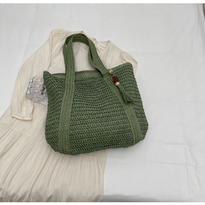 Close-up of olive green woven tote bag featuring beaded tassel and mesh texture detail