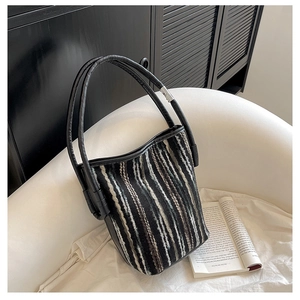 Detail einer gestreiften Tweed-Beuteltasche mit schwarzem Ledergriff und Metallringen