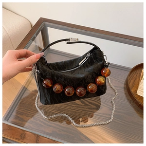 Detail van zwarte geplooide tas met amberkleurige kralen en zilveren ketting op glas