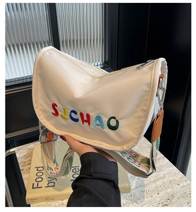 Detail of white half-moon canvas bag featuring colorful embroidery and floral wide strap