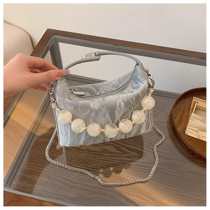Detail van de zilveren geplooide handtas met grote witte kralen en een fijne ketting