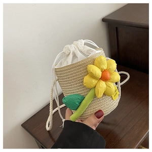 Detail of a beige straw bucket bag with a yellow flower and white drawstring closure