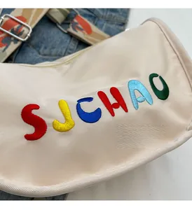 Detailed close-up of beige nylon crescent bag with rainbow embroidery and ethnic strap