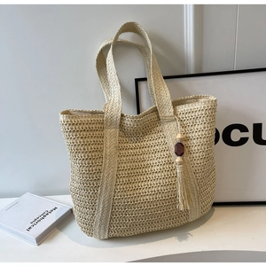 Close-up of woven straw tote bag featuring decorative wooden beads and beige tassels