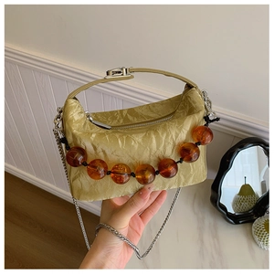 Detail van lichtgroene handtas met plooien, amberkleurige kralen en zilveren ketting
