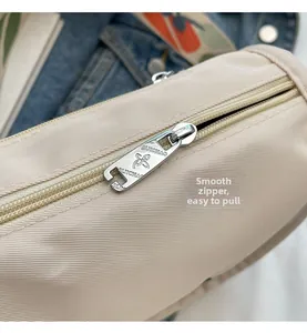Close-up of a smooth silver zipper with butterfly logo on a beige nylon crossbody bag