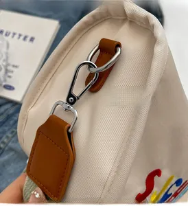 Close-up of silver metal clasp on beige fabric bag with colorful embroidery and brown strap