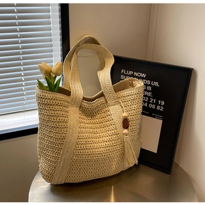 Detailed view of woven straw tote bag featuring wood beads and tassels for beach style