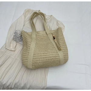 Detail of a large beige straw tote bag with decorative wooden bead tassels for beach summer